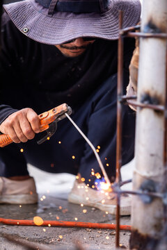 Selective focus to Male construction worker wearing sunglasses and bucket hat welding a steel structure at a job site. Glowing bright sparks fly off the electric metal arc welding process during outdo