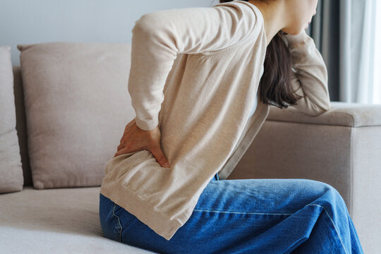Woman suffering from back pain while sitting on the couch at home, Health care and medical concept