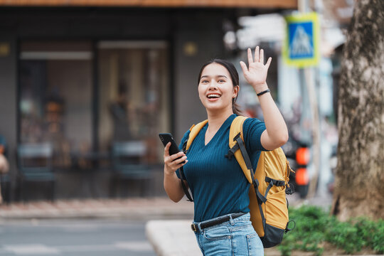 Young woman traveler waving while holding phone on street