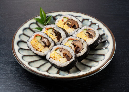 Japanese Futomaki Thick Sushi Rolls on Patterned Ceramic Plate on Dark Wooden Table