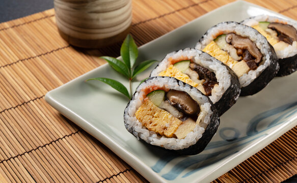 Japanese Futomaki Thick Sushi Rolls on Ceramic Plate with Tea Cup on Bamboo Mat