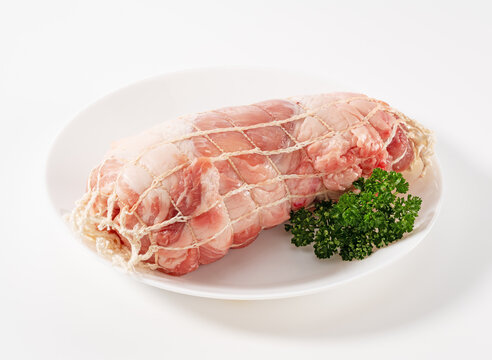 Raw Pork Shoulder Roast Tied in Meat Netting on White Plate with Parsley Isolated on White Background