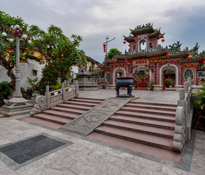 Exterior view of the Phuc Kien Assembly Hall, a historic Chinese temple with a stone incense burner and dragon stairs, located in the ancient town of Hoi An, Vietnam