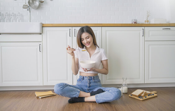 Portrait young beautiful asian woman relax sit on kitchen floor. Smile happy asian girl have breakfast cereal milk breadhome minimal lifestyle. Freelance small business asian owner sme work from home