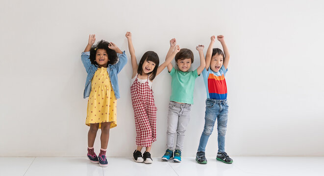 Four diverse asian black caucasian children standing together with raised arms, smiling and celebrating friendship, playfulness, childhood joy, and youthful energy back to school education.