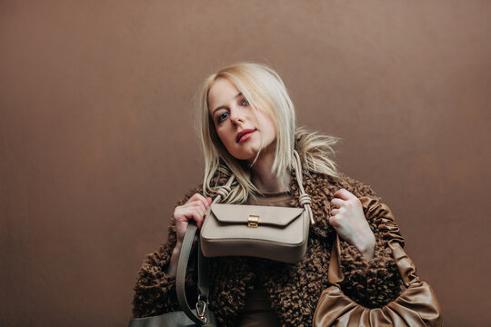 A stylish blonde woman wearing a teddy coat paired with vintage bags, standing against a rich brown background in shade Mocha Mousse