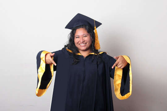 Young, dark-haired Latina woman dressed in a cap and gown is happy and excited to celebrate her graduation