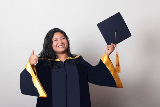 Young, dark-haired Latina woman dressed in a cap and gown is happy and excited to celebrate her graduation
