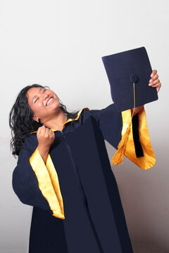Young, dark-haired Latina woman dressed in a cap and gown is happy and excited to celebrate her graduation