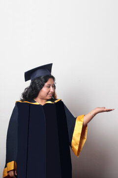 Young, dark-haired Latina woman dressed in a cap and gown is happy and excited to celebrate her graduation