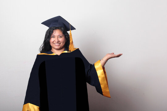 Young, dark-haired Latina woman dressed in a cap and gown is happy and excited to celebrate her graduation