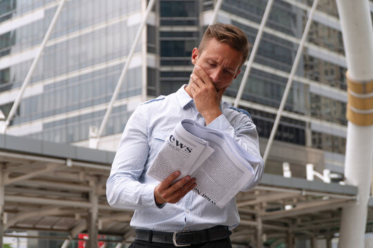 Stressed Caucasian businessman reading bad news in newspaper while standing outdoors in modern city. Economic crisis, financial problem, and corporate stress concept. Perfect for business articles.