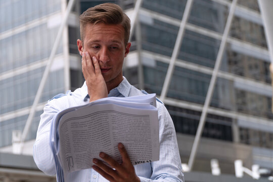 Stressed Caucasian man reading bad news in newspaper while standing outdoors in a modern city. Financial crisis, job loss, and stress concept. Perfect for business and economic articles.