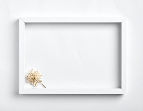 Minimalist white picture frame with a single dried flower on a white background.