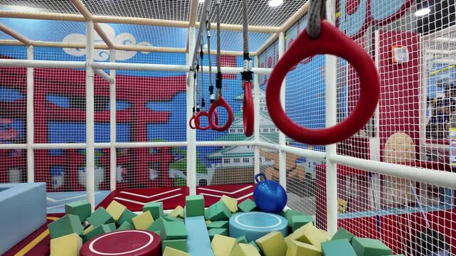 Colorful indoor playground obstacle course with gymnastics rings and foam pit for children recreation.
