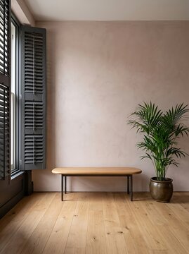 Minimalist interior corner with textured pink wall, light wood floor, wooden bench with black metal legs, potted palm plant in ceramic pot, and window with dark grey shutters letting in natural light