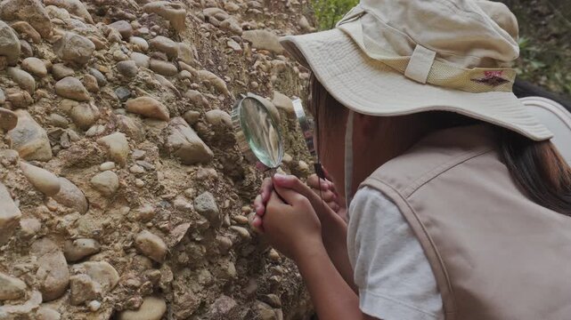 Asian mother and daughter looking through magnifying glass at geological rock stratum
