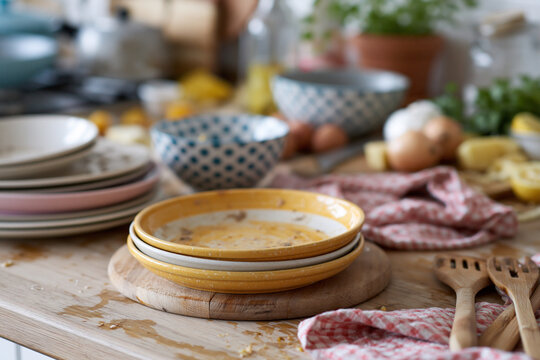 Stacked yellow bowls rest on a wooden trivet. Pink and red cloths lie nearby, slightly wrinkled. Wooden spoons sit beside the bowls, ready for use. Lemon slices and onions hint at recent prep
