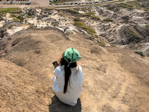 Woman sitting on hoodoo cliff overlooking Badlands valley, Drumheller Alberta