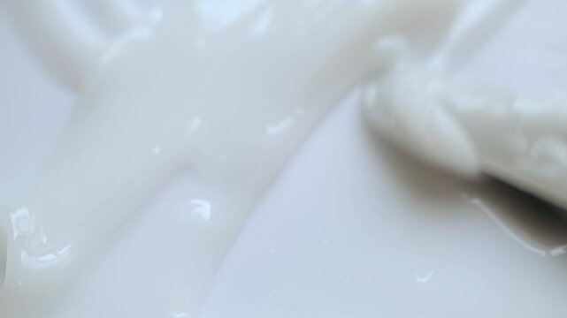 Extreme close-up of spatula stirring and spreading white cosmetic cream in slow motion