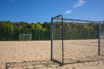 Beach Soccer Goal on Sandy Recreational Sports Field. A full-size beach soccer goal with a net stands on a sandy outdoor sports field surrounded by green woodland. The empty goal and open sandy playin © Nadiia