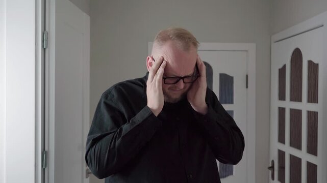 Caucasian man in a dark shirt presses his temples and winces, acting out.