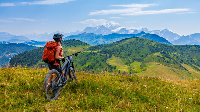 Woman mountain biker admiring the view of mont blanc from a green alpine ridge