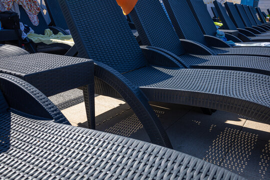 Pattern of Poolside Lounge Chairs with Strong Sunlight and Shadows. Close-up view of multiple dark poolside lounge chairs arranged in overlapping rows. Strong sunlight creates pronounced shadows acros