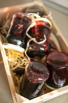 Close up of organic wild blueberry jam in a rustic wooden box. A straight-on close-up shot of homemade wild blueberry jam jars nestled chaotically inside a decorative wooden crate. The jars are covere