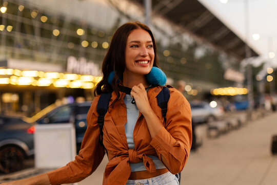 Joyful woman tourist wearing comfortable neck pillow and carrying backpack while preparing to board flight at airport