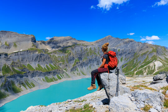 Woman hiker sitting on a rock overlooking a turquoise mountain lake in the swiss alps- adventure, travel, freedom concept