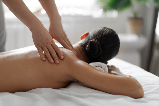 Lady lying face down on massage table, enjoying soothing back massage in tranquil spa with peaceful atmosphere