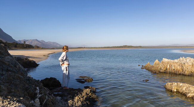 young woman standing on rock as she looks out at Grotto lagoon, Hermanus, South Africa