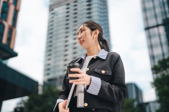Portrait of executive business asian leader solopreneur woman holding laptop and coffee cup city building background