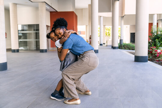 Happy mother giving piggyback ride to her daughter on first day back to school, expressing love and support