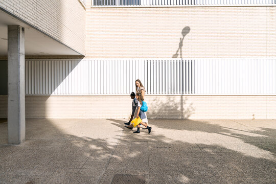 Multiethnic mothers walking with two girls wearing school uniforms and backpacks on their first day back to school