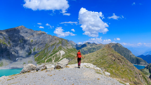 Woman hiker walking along a mountain ridge above turquoise alpine lakes in the swiss alps