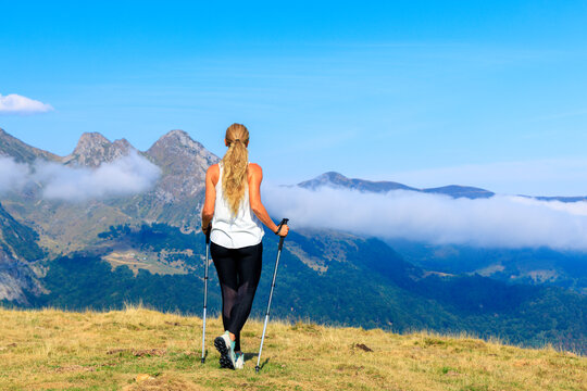 Woman hiking with trekking poles above the clouds overlooking mountain peaks