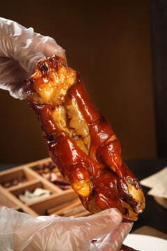Glazed Marinated Pork Knuckle with Golden Caramelized Coating Held by Chef in Gloves