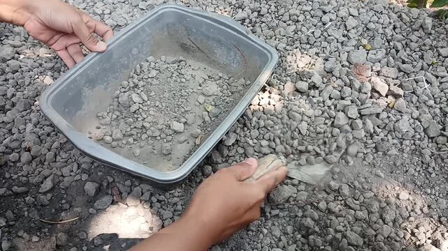 Worker mixing cement powder and gravel stone in plastic tray using trowel for DIY construction project