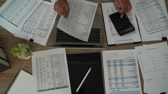 Accountant reviewing financial reports over laptop with calculator, tablet, printed documents for accounting, tax preparation, audit, bookkeeping, financial planning.