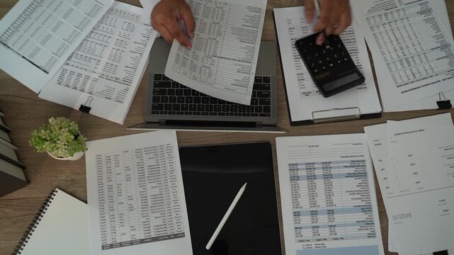 Accountant reviewing financial reports over laptop with calculator, tablet, printed documents for accounting, tax preparation, audit, bookkeeping, financial planning.