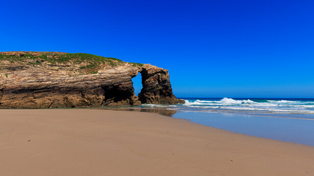 Natural rock arch on a sandy beach with waves crashing on the coast of galicia spain