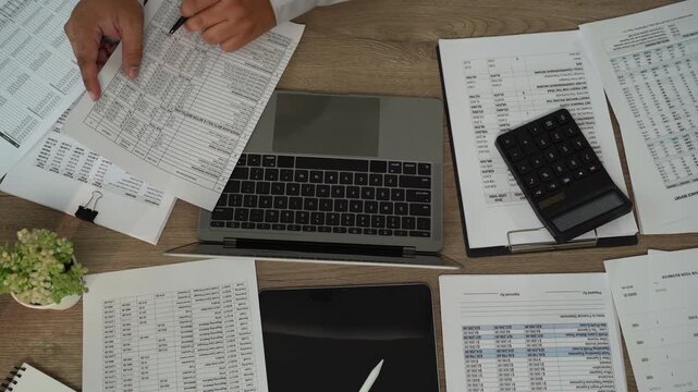 Accountant checking financial reports with pen beside laptop, calculator, tablet for accounting, tax preparation, audit, bookkeeping, financial planning.
