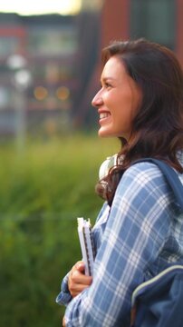 Happy female student walking across college campus, smiling and enjoying pleasant atmosphere while carrying books and wearing backpack, 4K, vertical