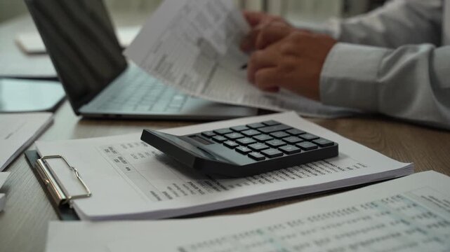 Accountant checking financial reports with pen beside laptop, calculator, tablet for accounting, tax preparation, audit, bookkeeping, financial planning.