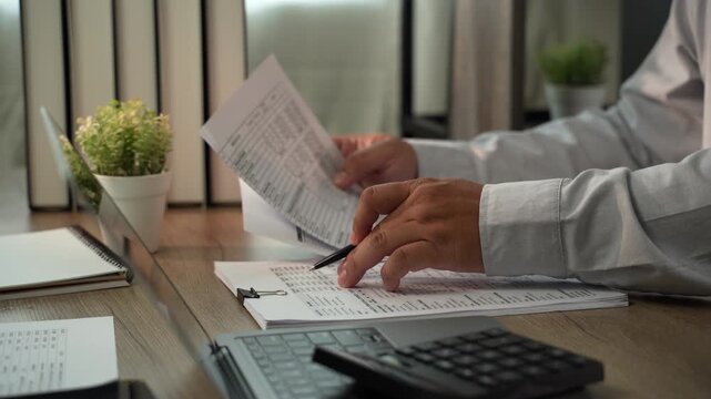 Accountant pointing at financial report with pen beside laptop and calculator for accounting, tax preparation, audit, bookkeeping, financial planning.