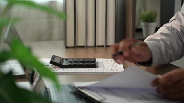 Accountant pressing calculator with pen on financial documents for tax preparation, accounting, audit, bookkeeping, financial planning in office.