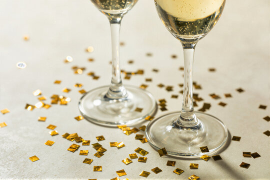 Two champagne flutes with gold confetti on light surface