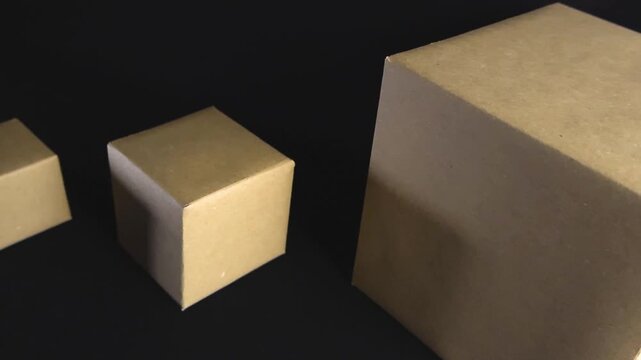 Smooth gliding shot moving past several brown cardboard boxes of different sizes arranged in a row on a plain black background, representing concepts like logistics, shipping, and packaging